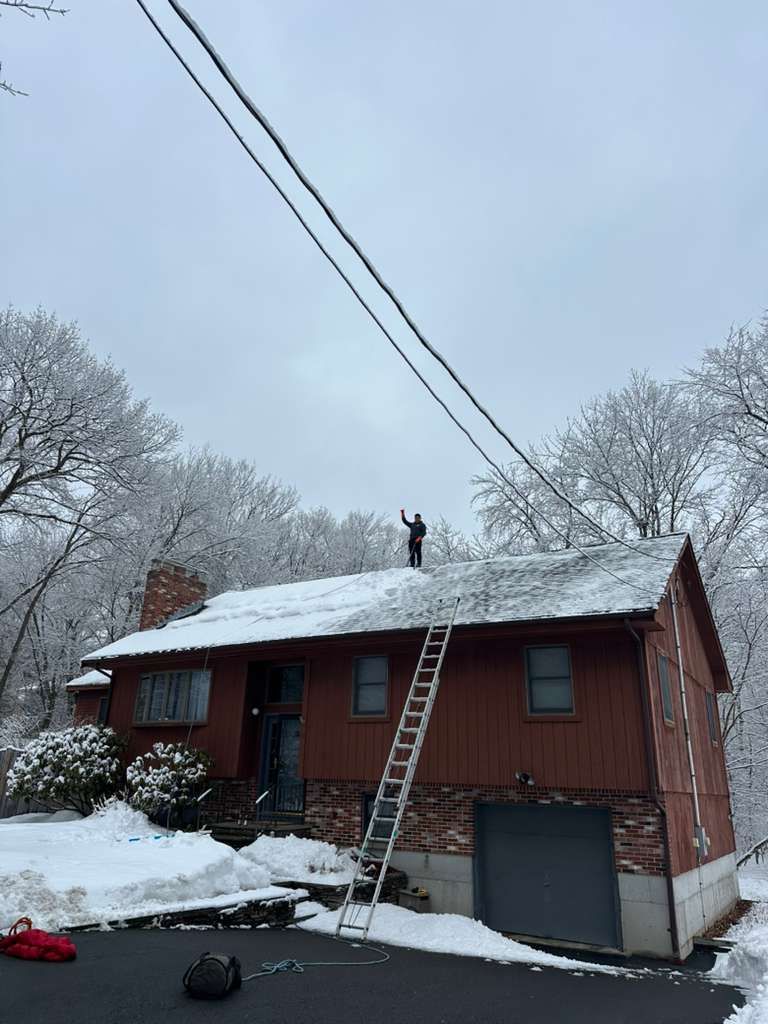 Red house with snow-covered roof, ladder to the roof, and a person standing near the peak.