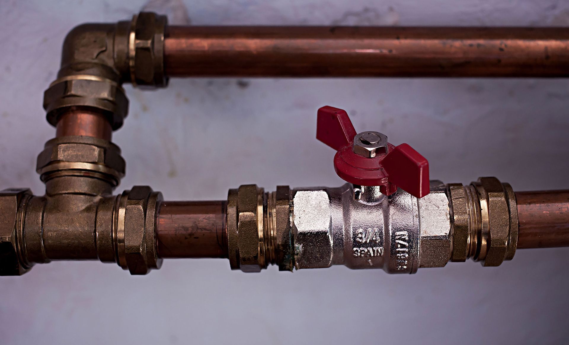 Copper pipes with brass fittings and a red-handled valve.