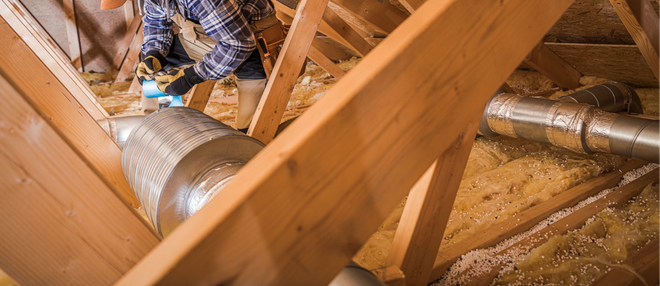 Person installing ductwork in an attic, wooden beams visible.