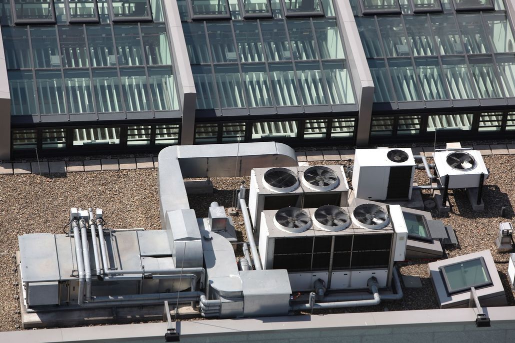 Rooftop HVAC units with fans and vents, set against a backdrop of a building with a glass roof.
