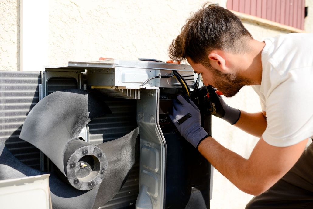 Man in gloves, repairing an air conditioning unit outside, working with wires.