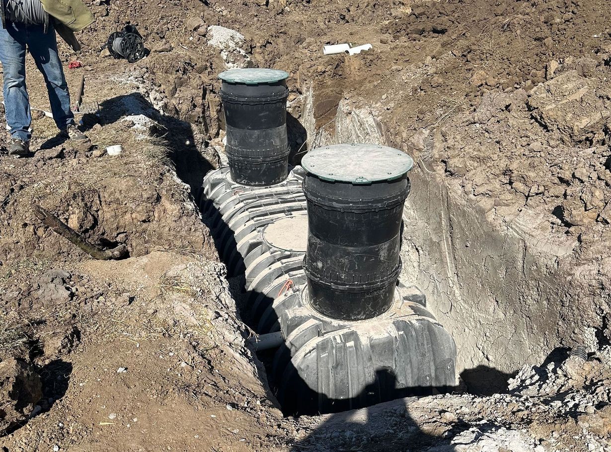 Septic system installation: two black access points and a connected perforated chamber in a dirt trench.