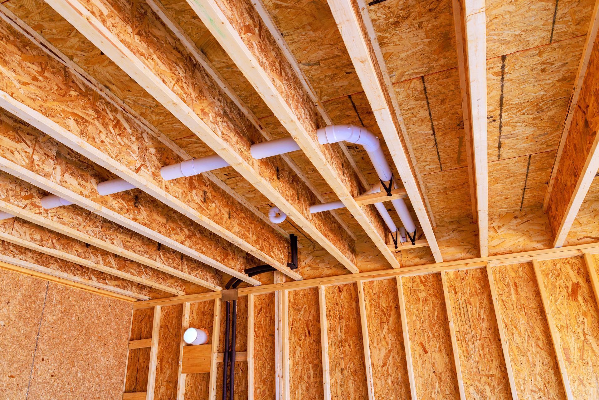 Interior view of a building under construction, showing exposed wooden beams, OSB sheathing, and plumbing.