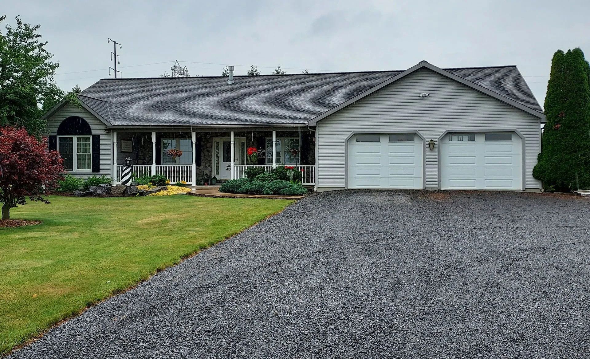 A single-story, light-colored house with a covered front porch, an attached two-car garage, and a gravel driveway.