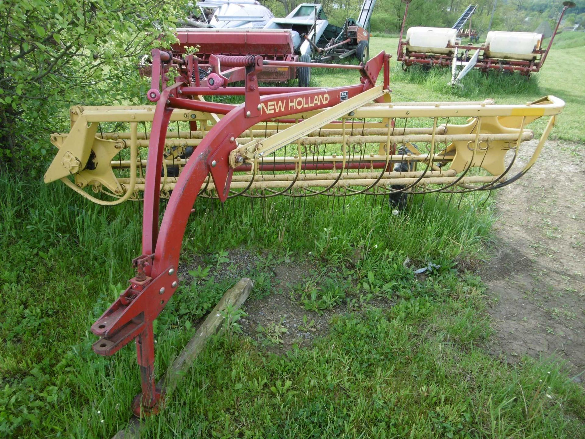 A red and yellow New Holland hay rake parked in a grassy field.