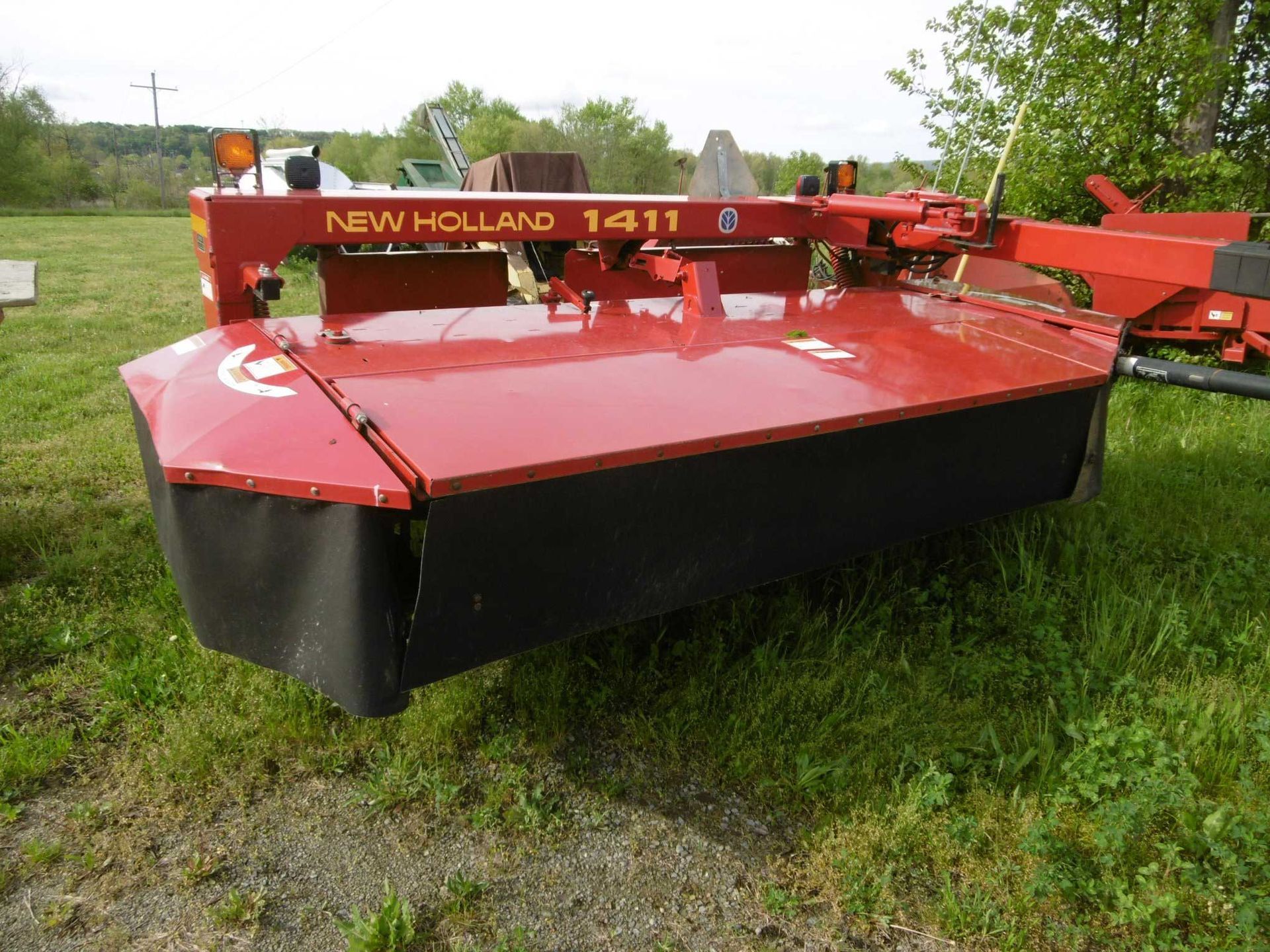 A bright red New Holland 1411 disc mower conditioner parked on a grassy field.