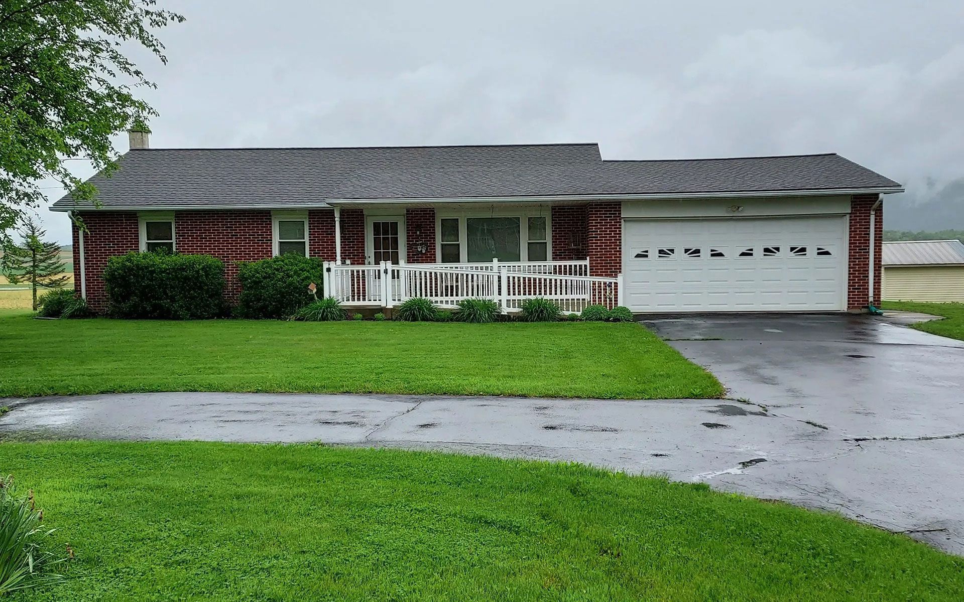 A single-story log cabin home with a white porch railing, a white garage door, and a paved driveway, set against a lawn.