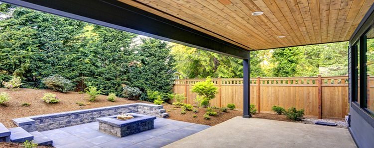 Patio with fire pit, lush greenery, wooden fence, and wood-paneled ceiling.