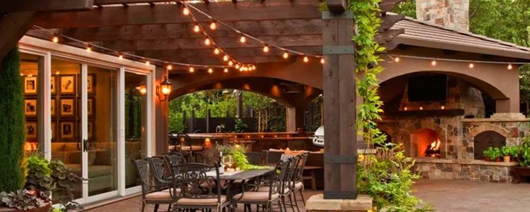 Outdoor patio with string lights, fireplace, dining set, and arbor.