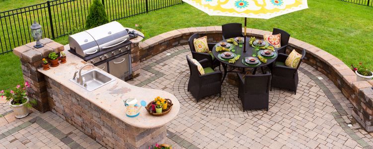Outdoor patio with grill, sink, and dining table with umbrella on brick pavers.