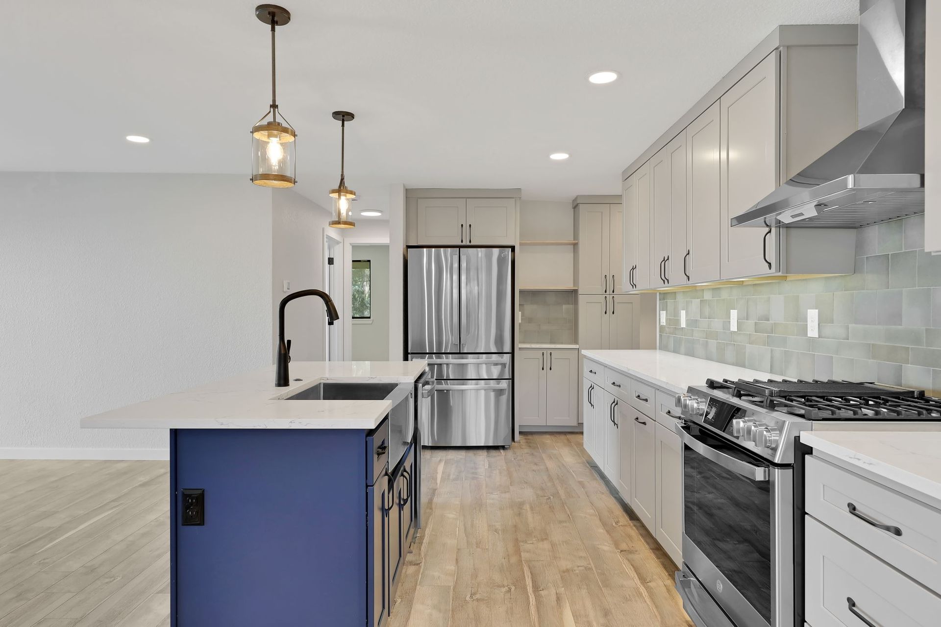 Modern kitchen: white cabinets, blue island, stainless steel appliances, pendant lights.