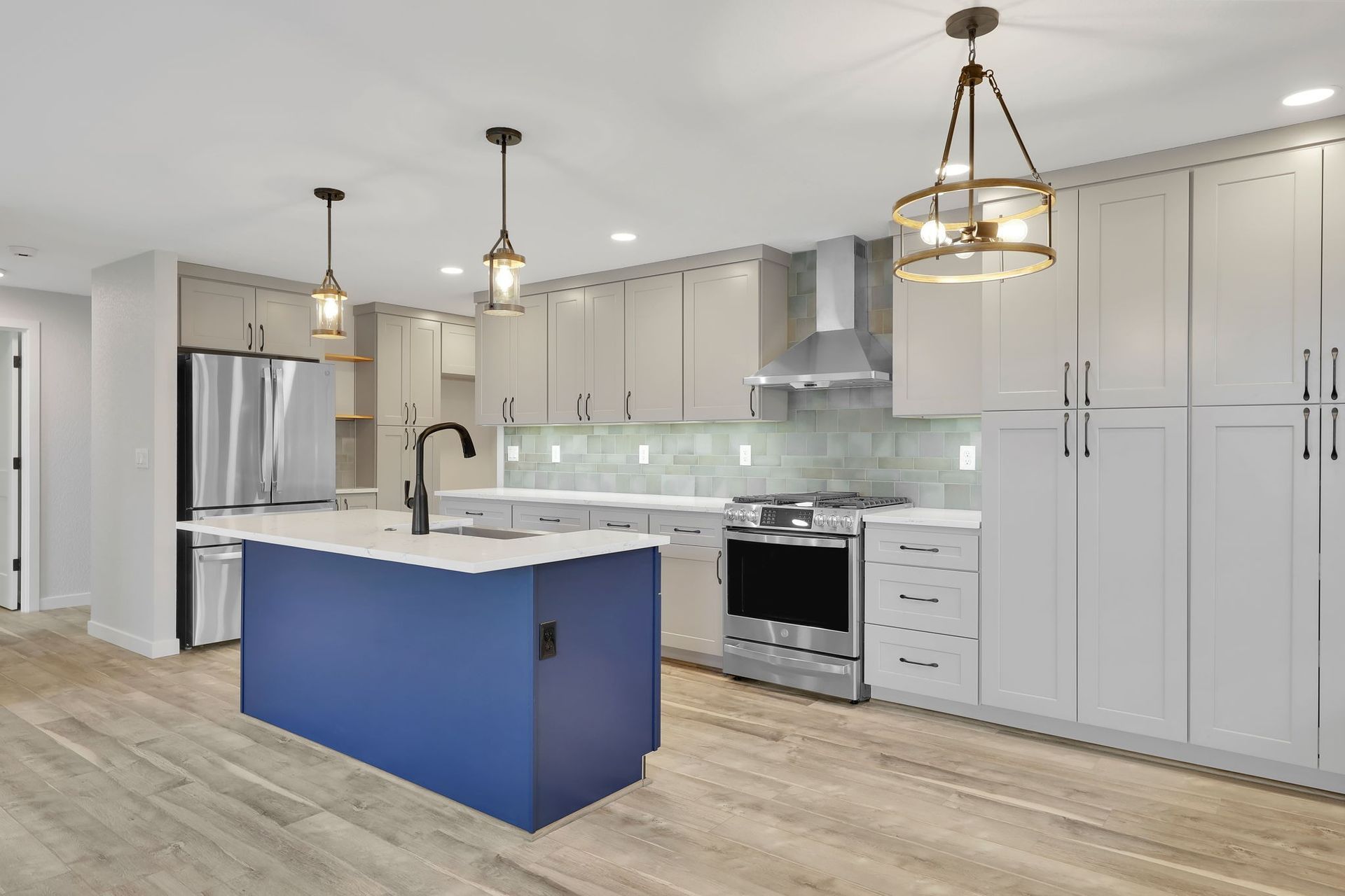 Modern kitchen with blue island, light gray cabinets, stainless steel appliances, and wood flooring.