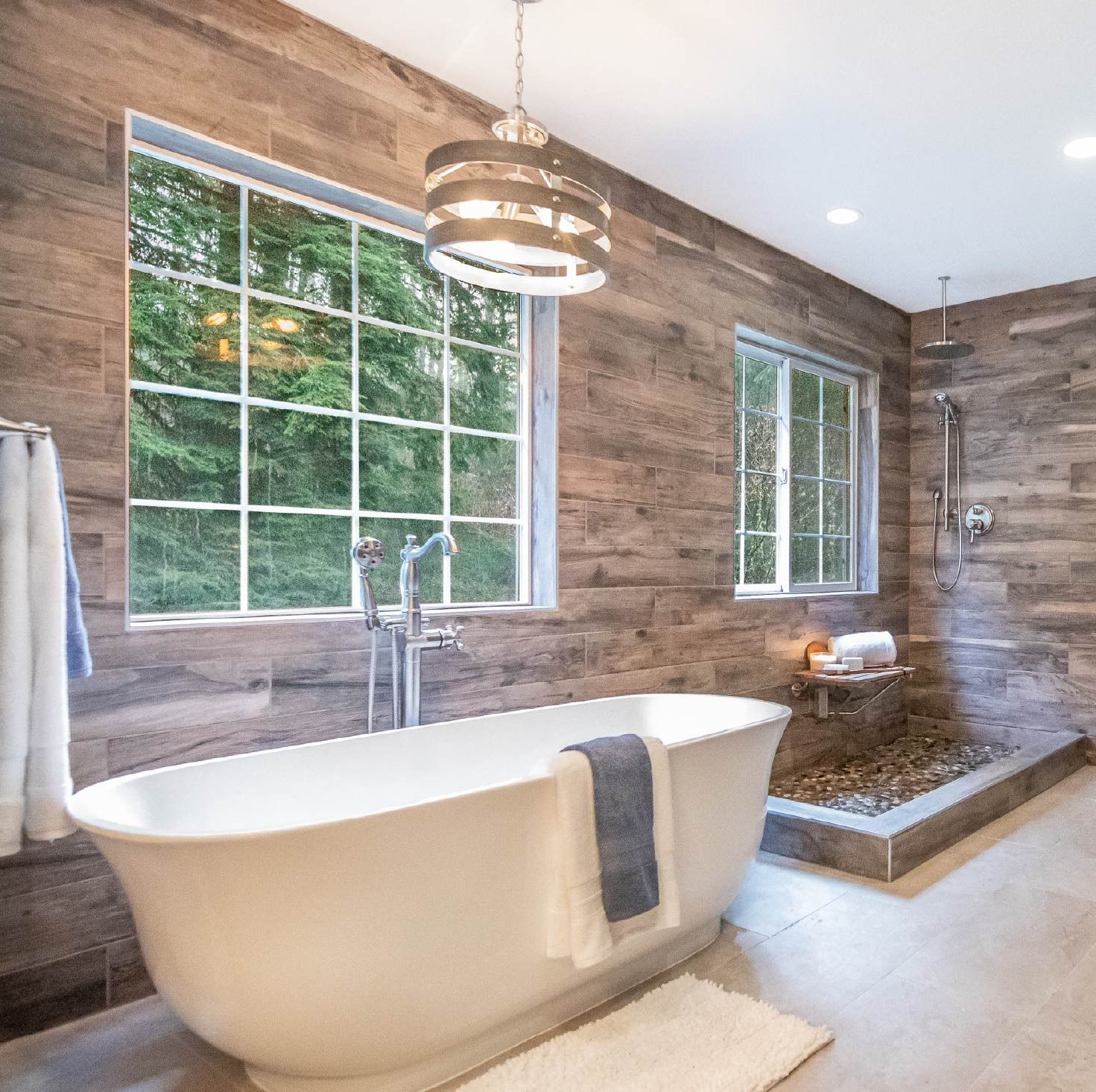 Bathroom with a white soaking tub, wood-paneled walls, and large windows overlooking trees.