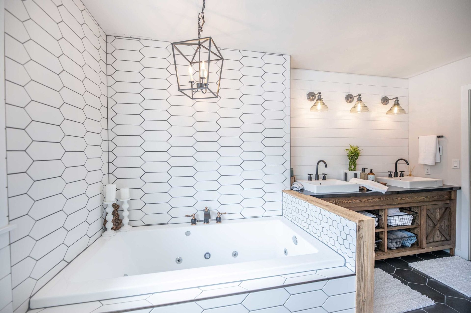White and black tiled bathroom with tub, double vanity, and geometric light fixture.