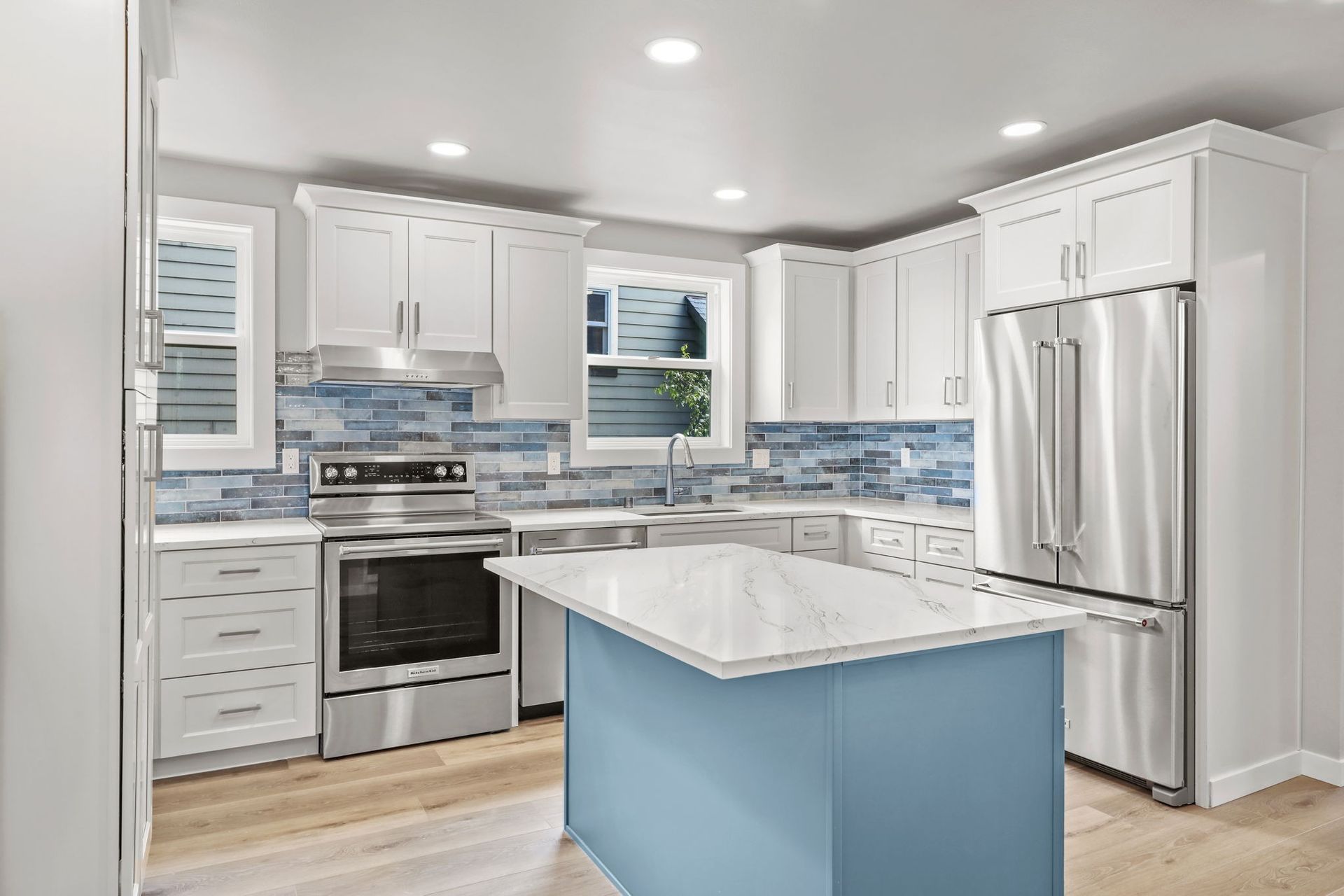 Modern kitchen with white cabinets, blue backsplash, stainless steel appliances, and a blue island with a white countertop.