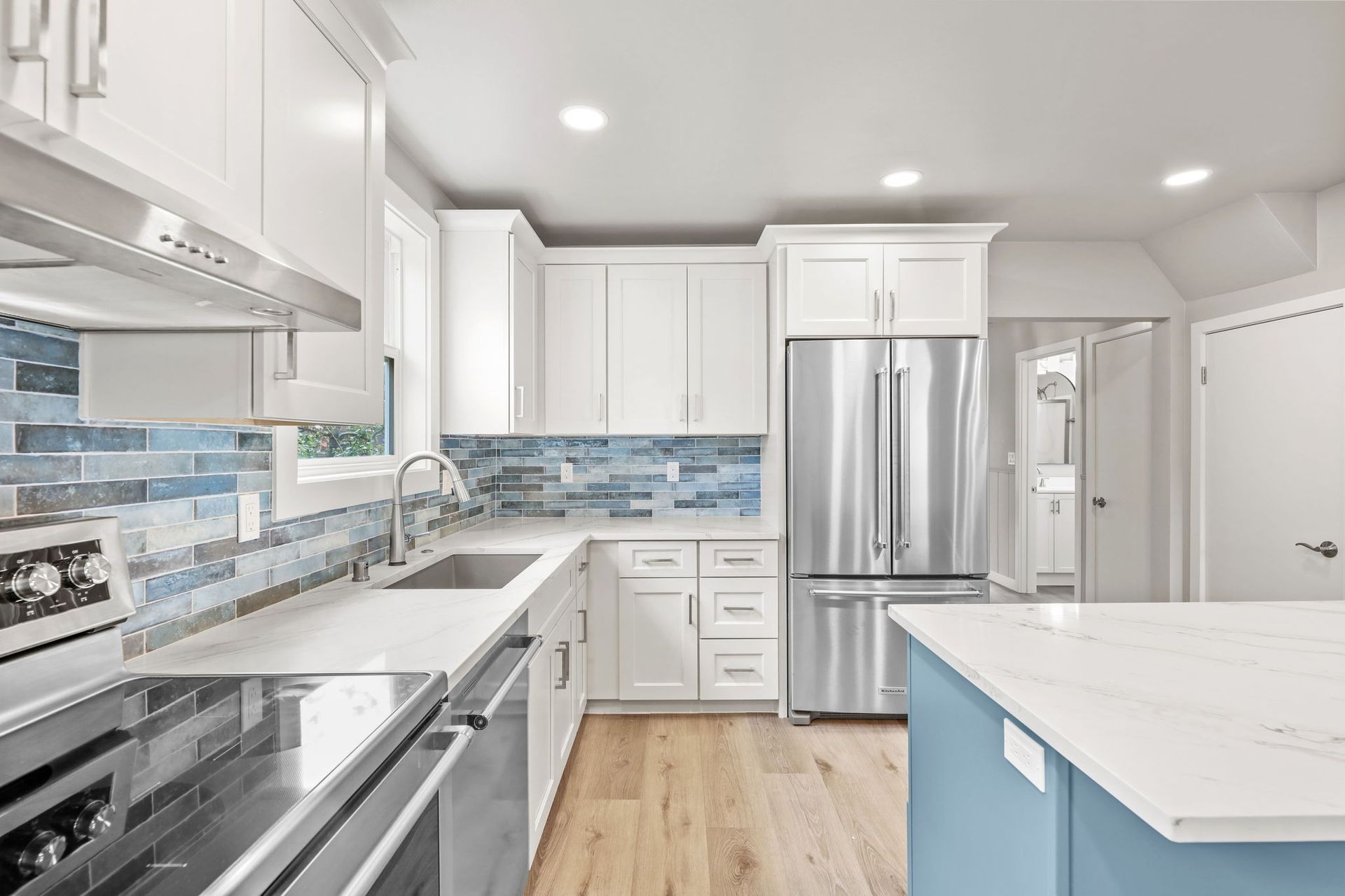 Bright kitchen with white cabinets, stainless steel appliances, and blue tile backsplash.