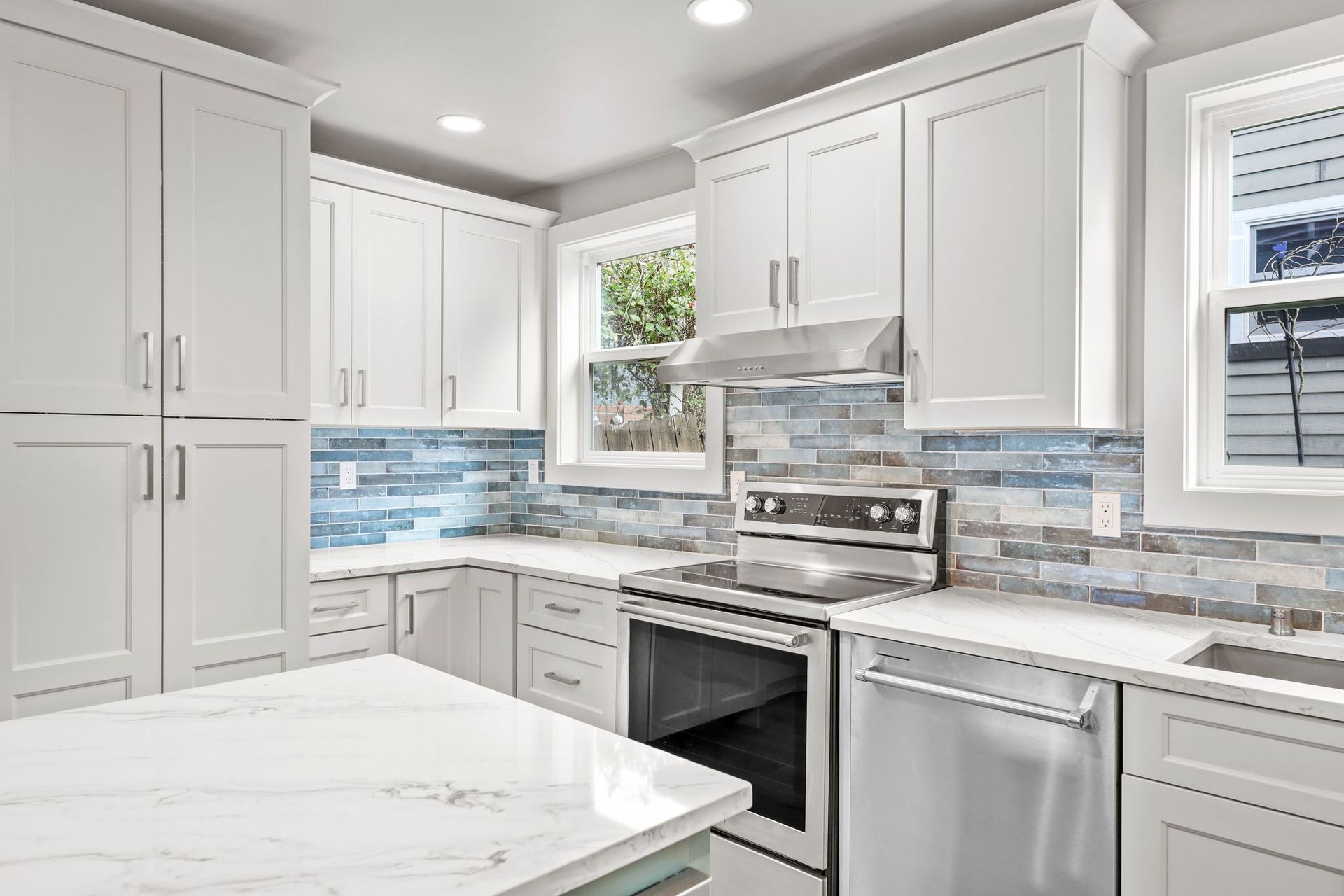 White kitchen with marble counters, stainless steel appliances, and blue tile backsplash.
