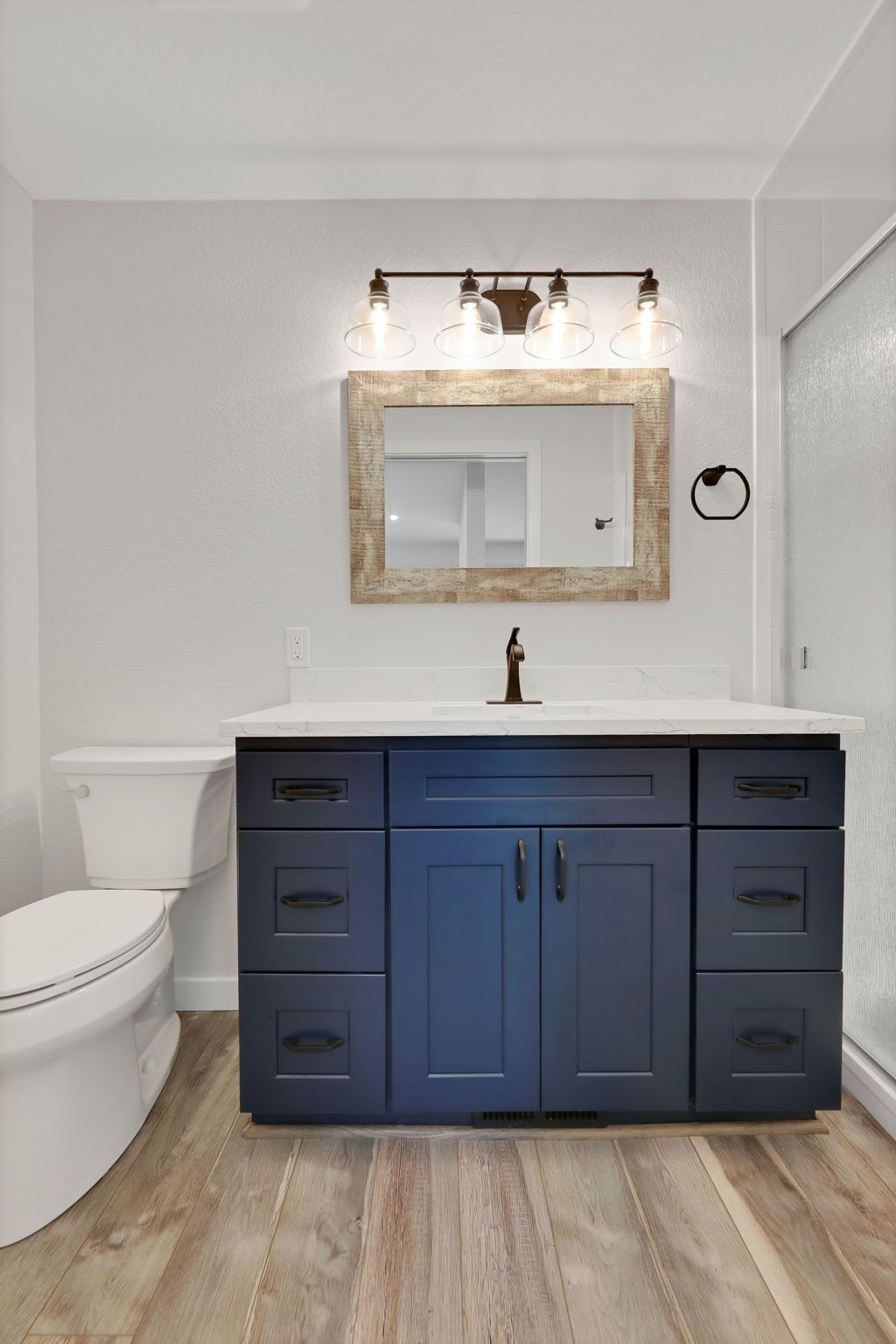 Blue bathroom vanity with white countertop, a light fixture, and a wooden framed mirror.