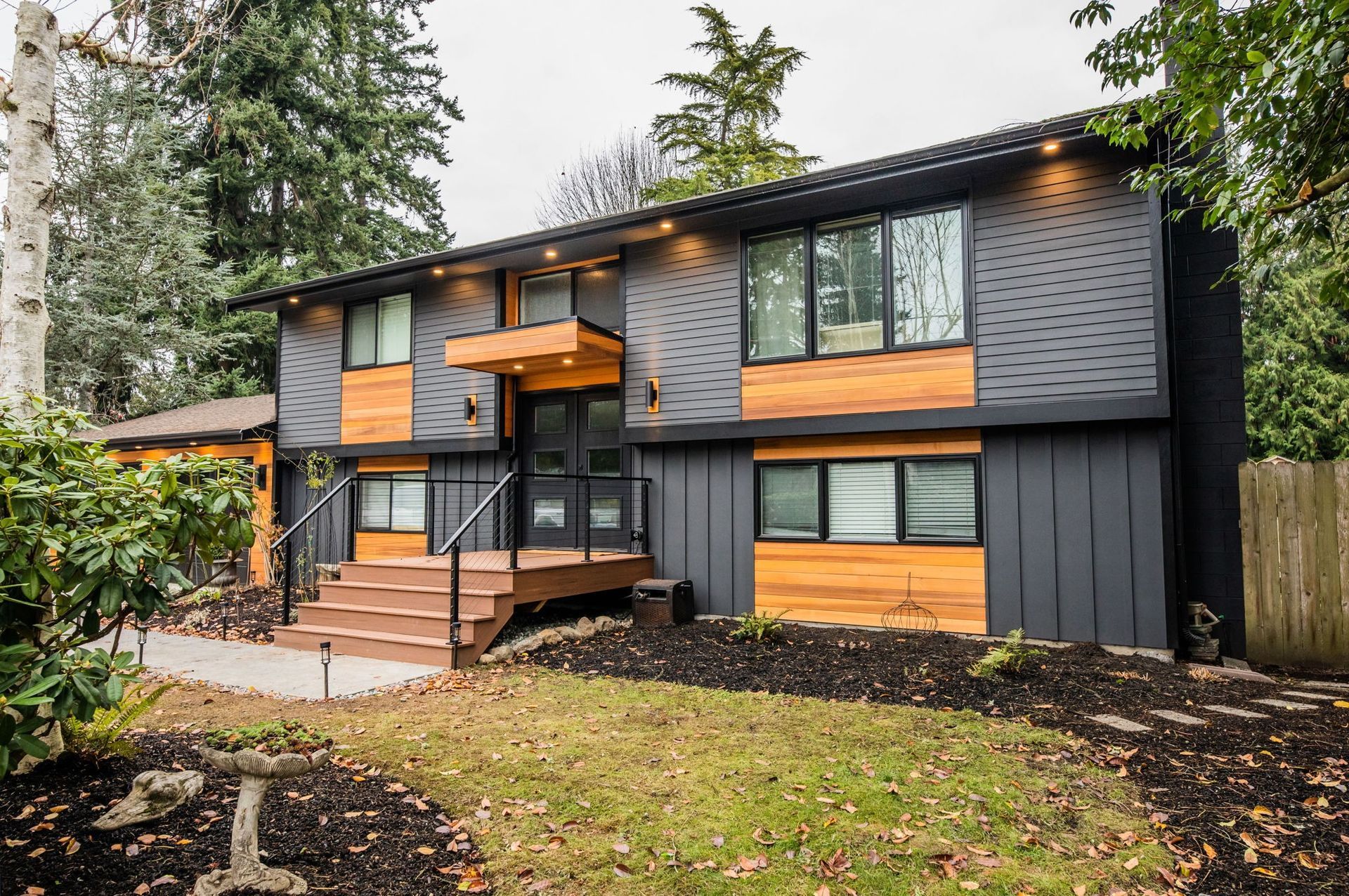 Modern two-story house with dark gray siding, wood accents, and a front porch on a grassy lawn.