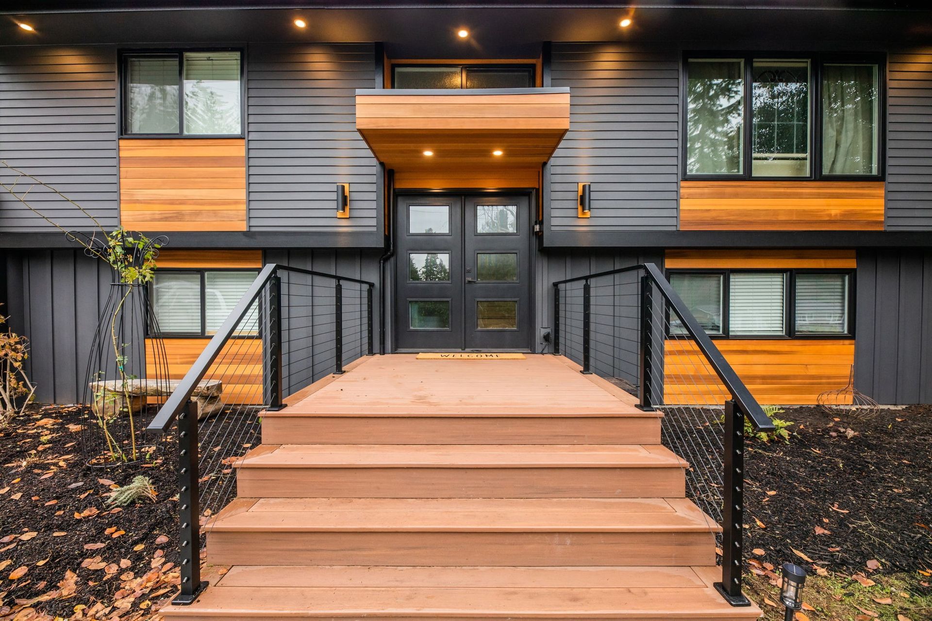 Modern home exterior with wooden steps, dark gray siding, and a wooden front door canopy.
