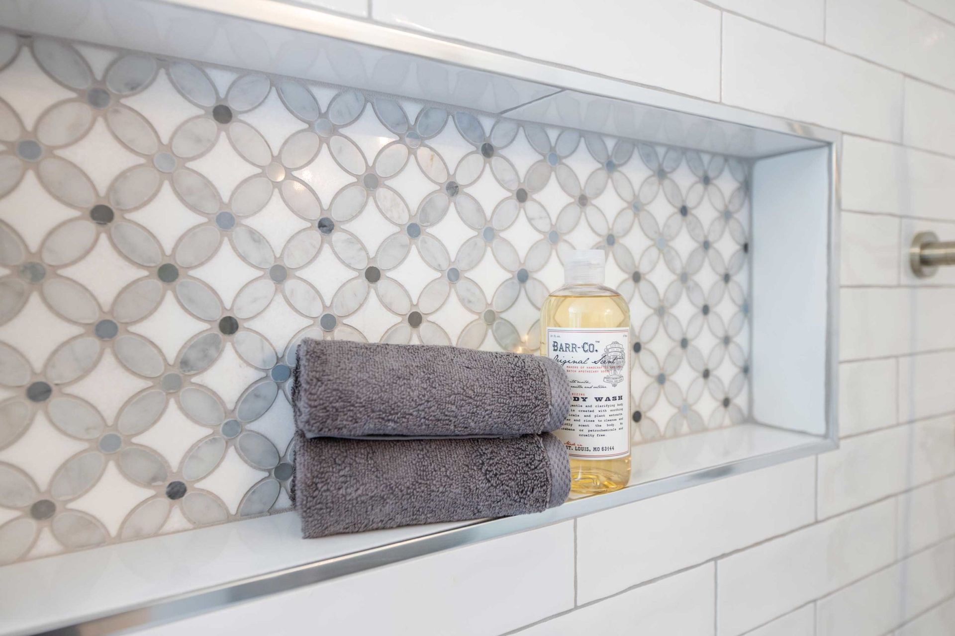 Recessed shower shelf with gray towels, soap, and flower-patterned tile.