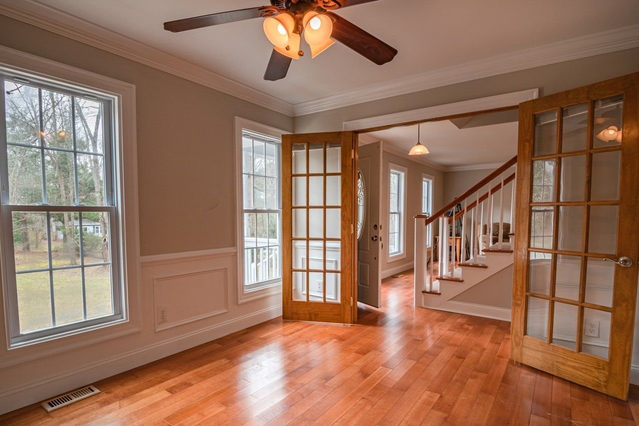 Empty room with wood floors, two windows, French doors, and a staircase.