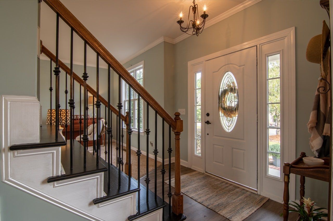Entryway with staircase, white door, and side windows, light green walls, brown and black railing, and dark wood floor.