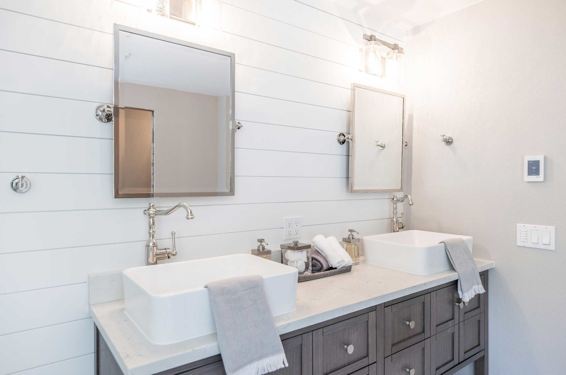 Bathroom with white shiplap wall, two vessel sinks, gray cabinets, and silver fixtures.