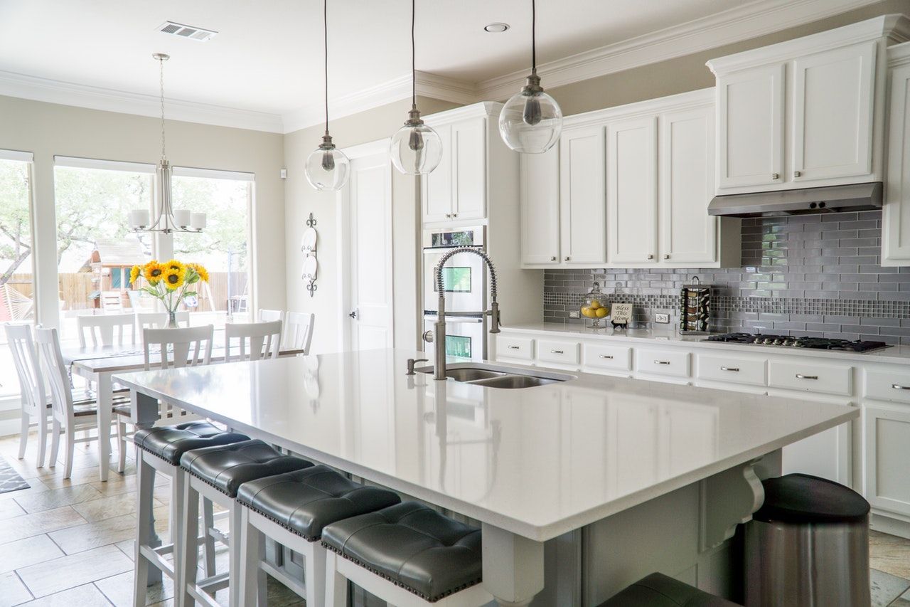 White kitchen with island, seating, white cabinets, stainless steel appliances, and dining table.