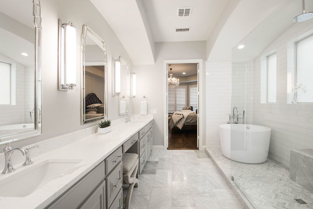 Bright, modern bathroom with double vanity, freestanding tub, and open doorway to the bedroom.
