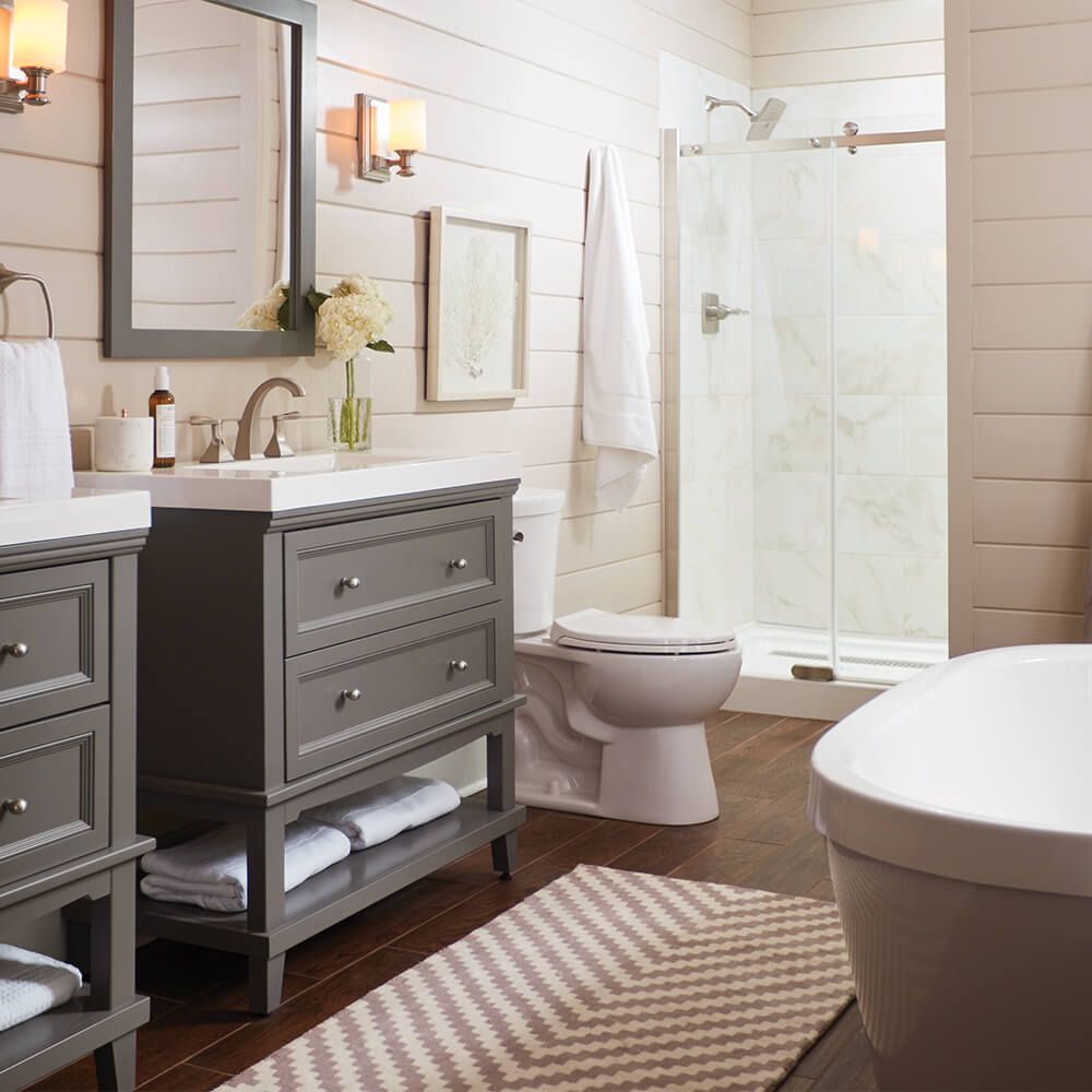 Bathroom with gray vanity, white fixtures, wood floor, and a chevron rug.