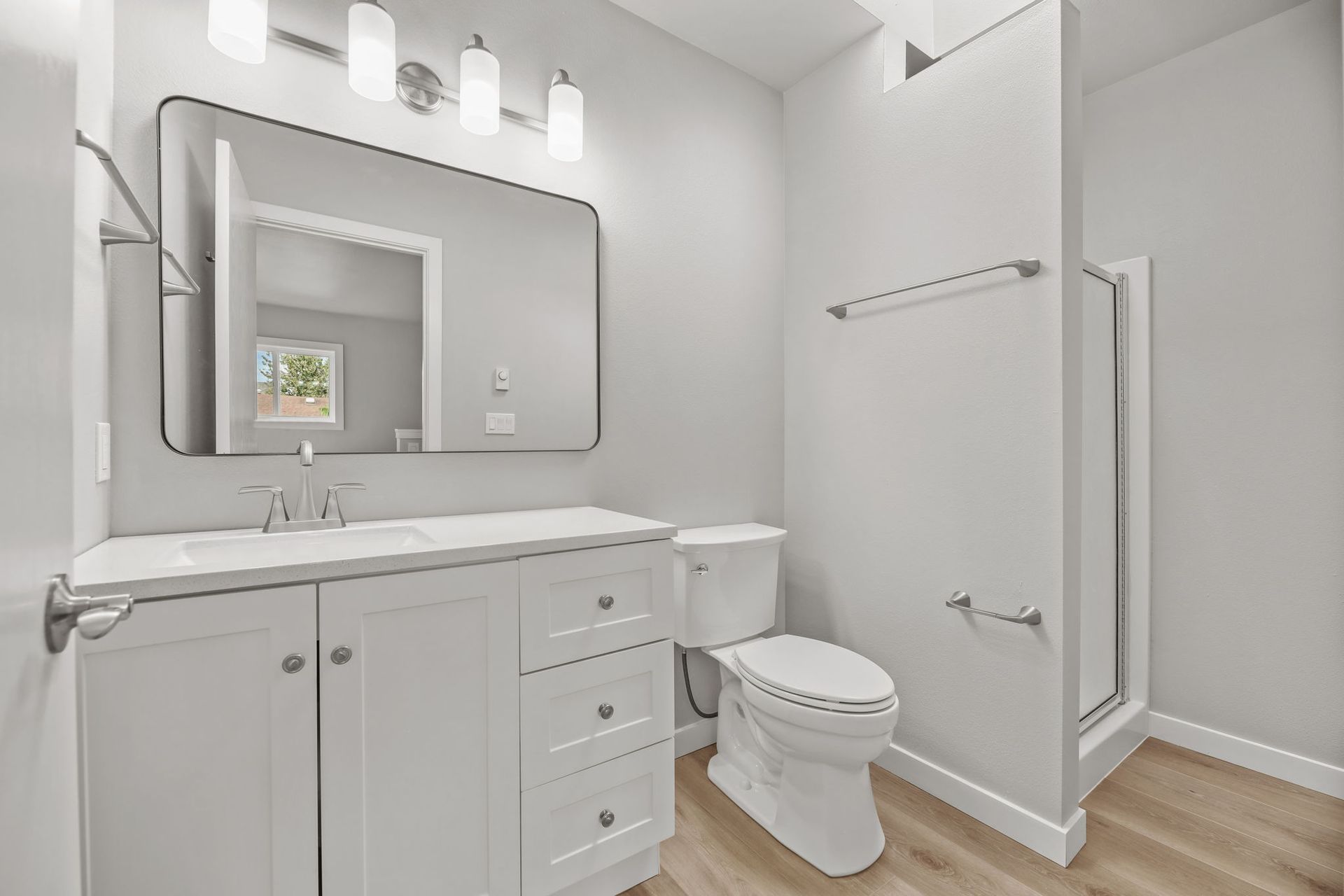 White bathroom with vanity, toilet, shower, and mirror.