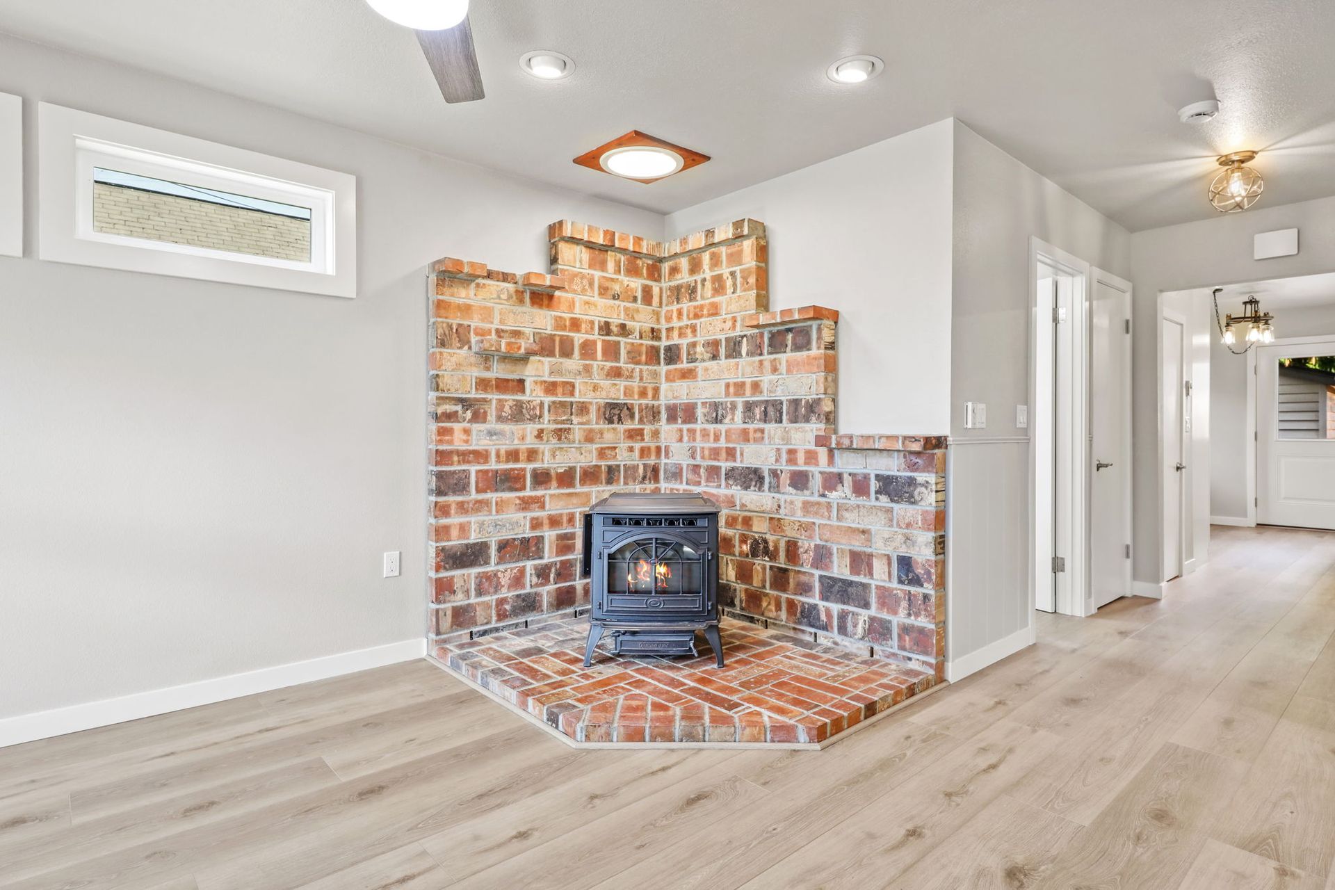 Fireplace with brick surround and wood-look flooring in a light-filled room.