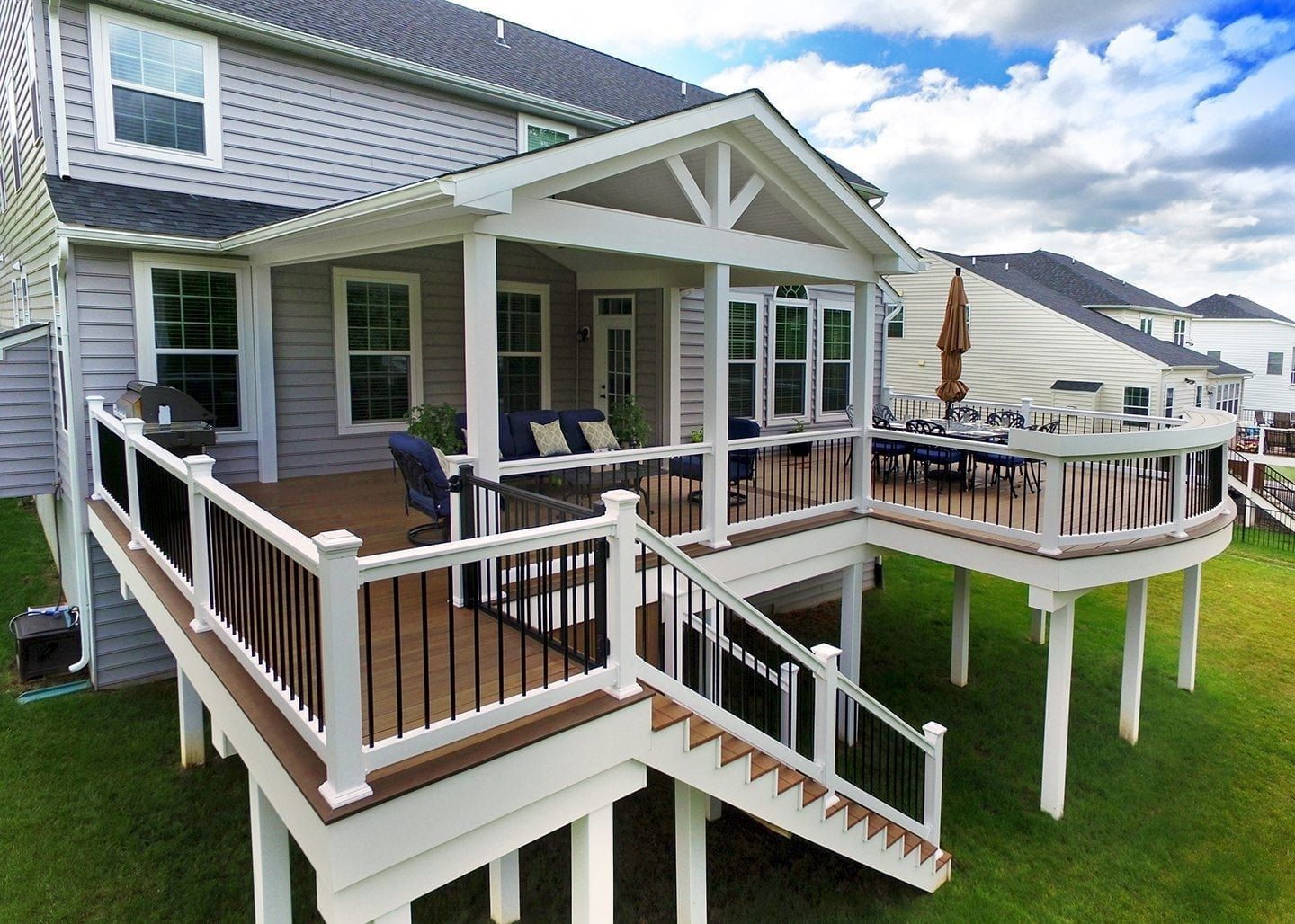 Two-level deck attached to a gray house, with a covered seating area, brown and white railings, and stairs.