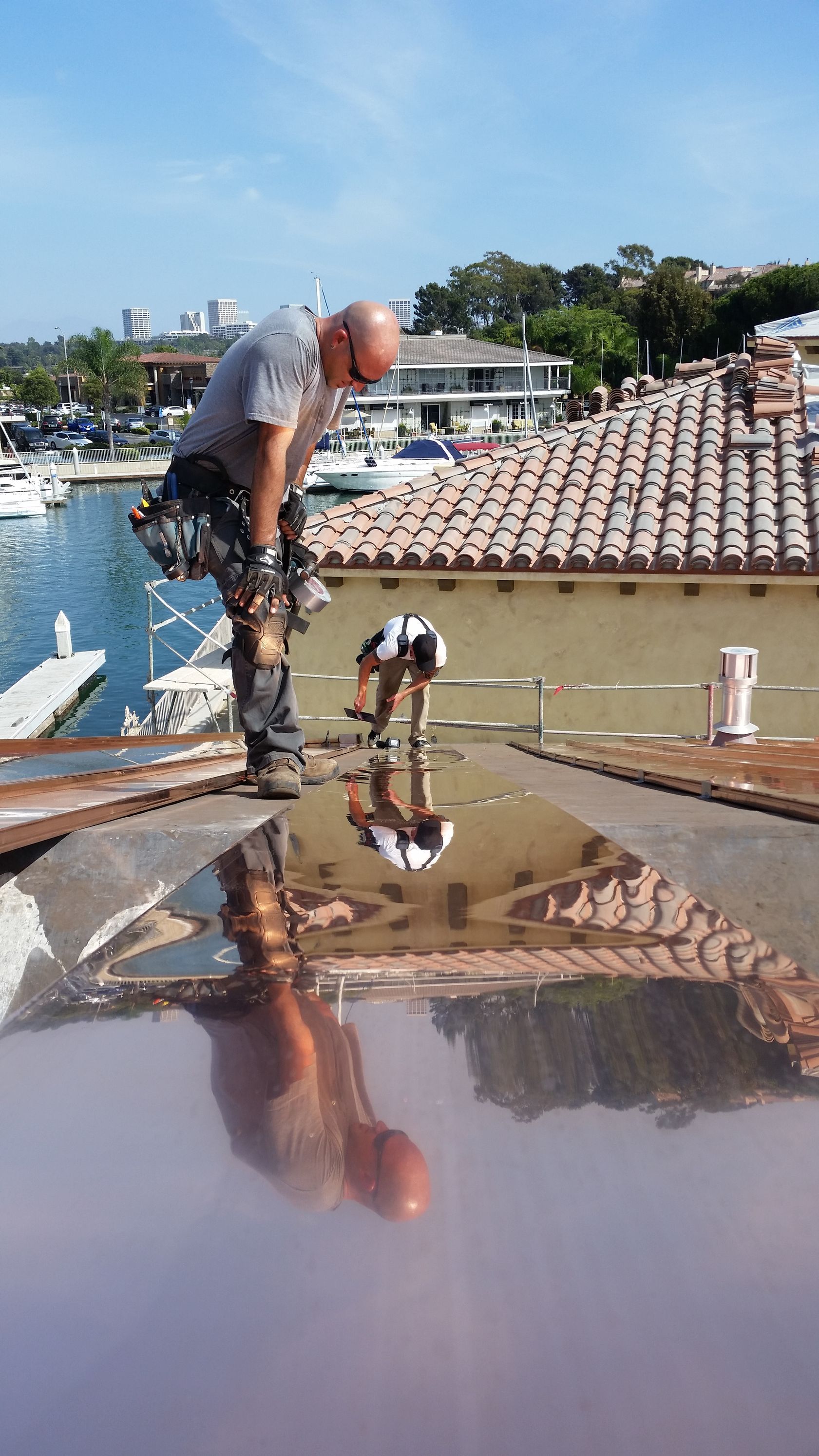 A man is working on the roof of a building and his reflection is in the water.