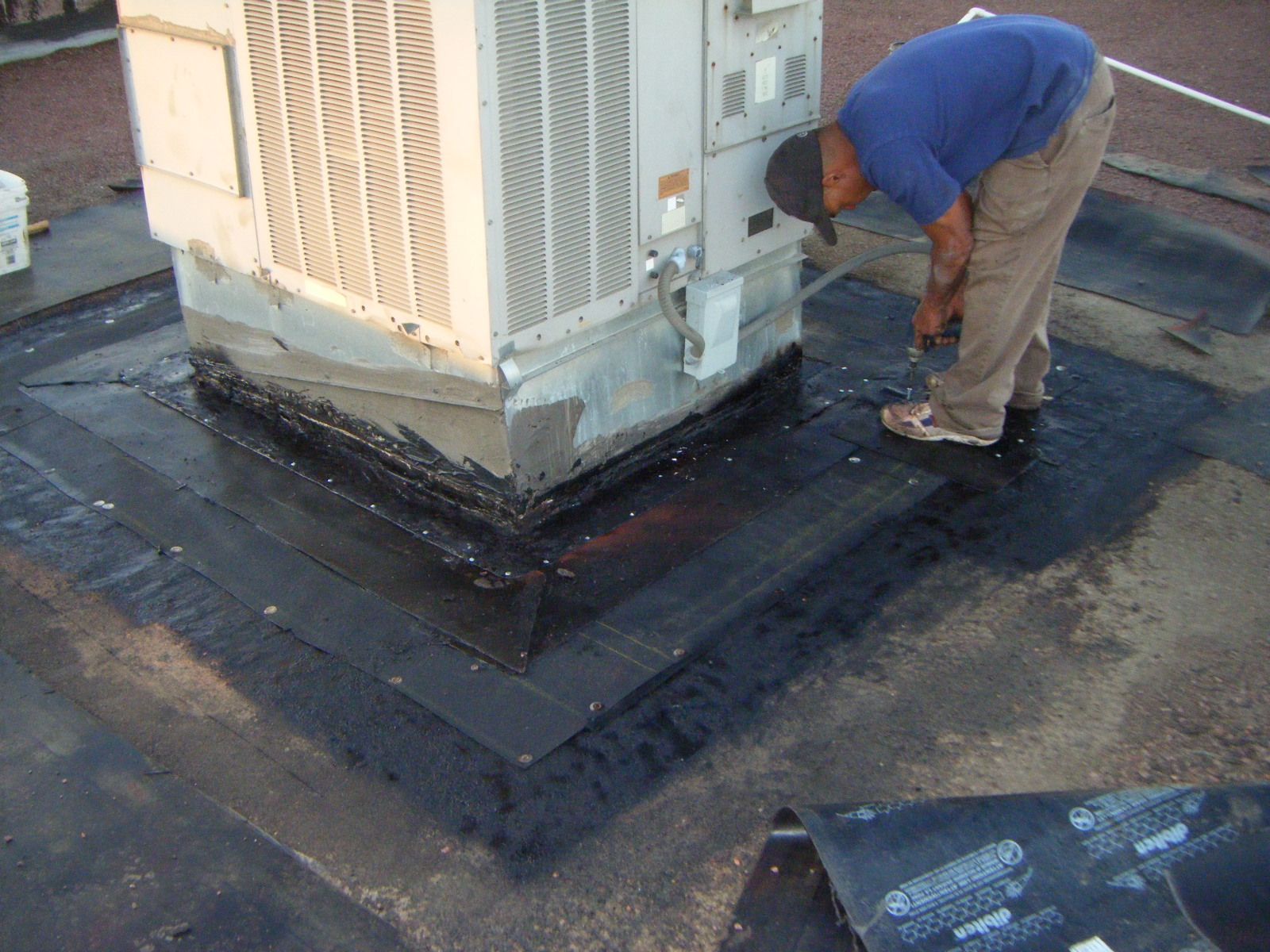 A man is working on an air conditioner on a roof