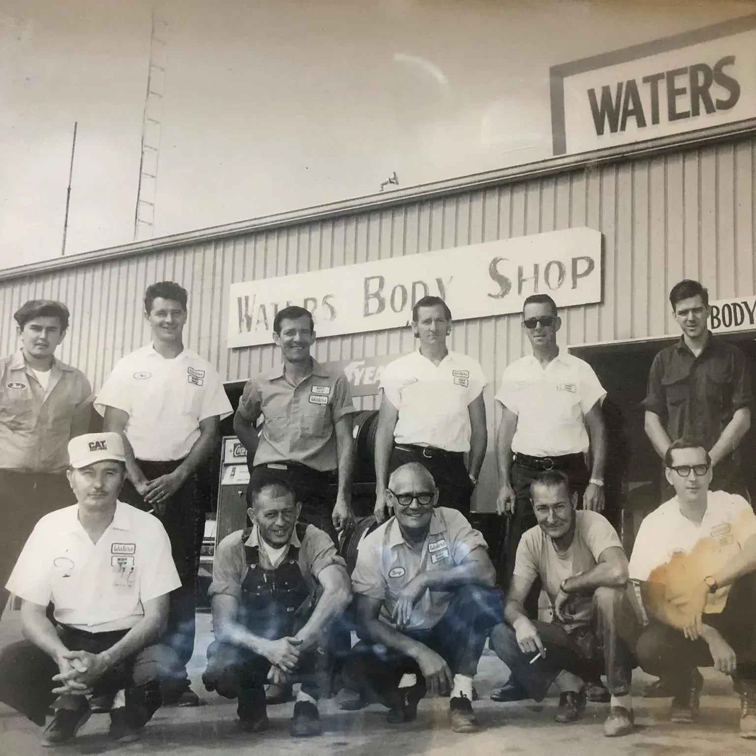 Group of people posing outside a storefront with a “Waters” sign and “Massey’s Bo Shop” banner.