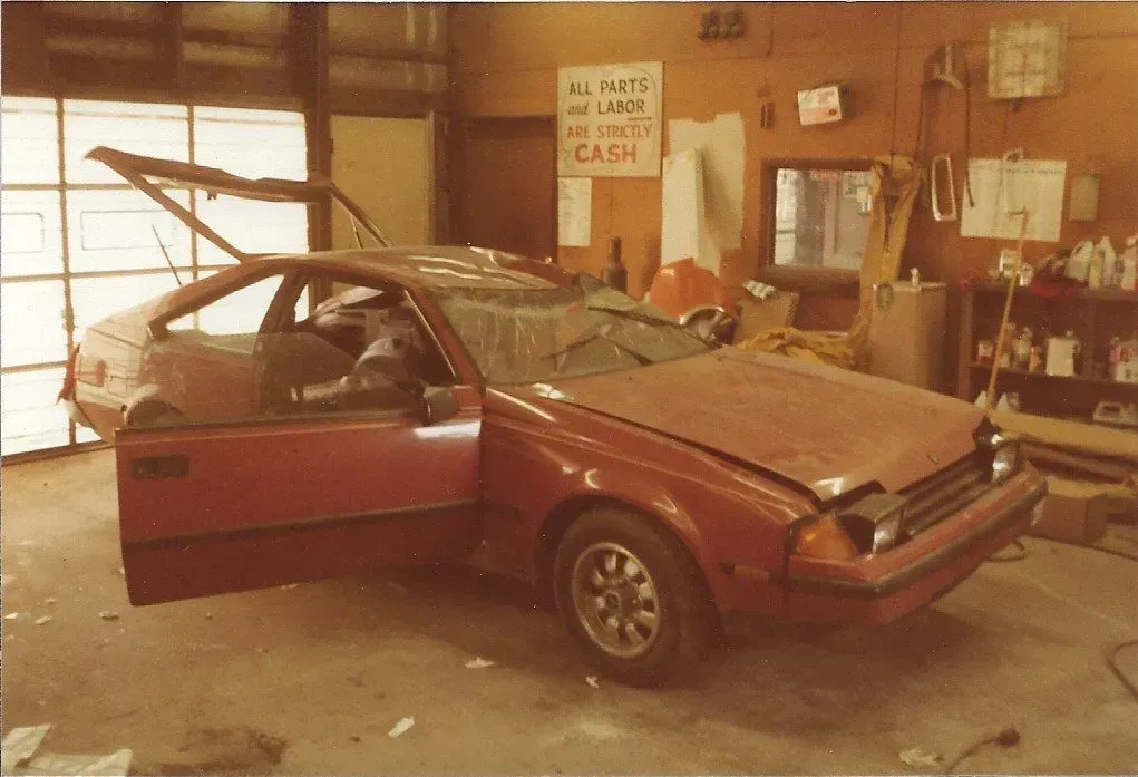 Damaged red car in a garage, with the driver’s door open and a front end crumpled.