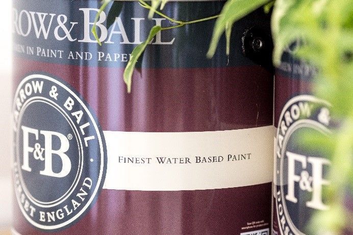 Close-up of Farrow & Ball paint cans, burgundy and white labels, a plant in the background.