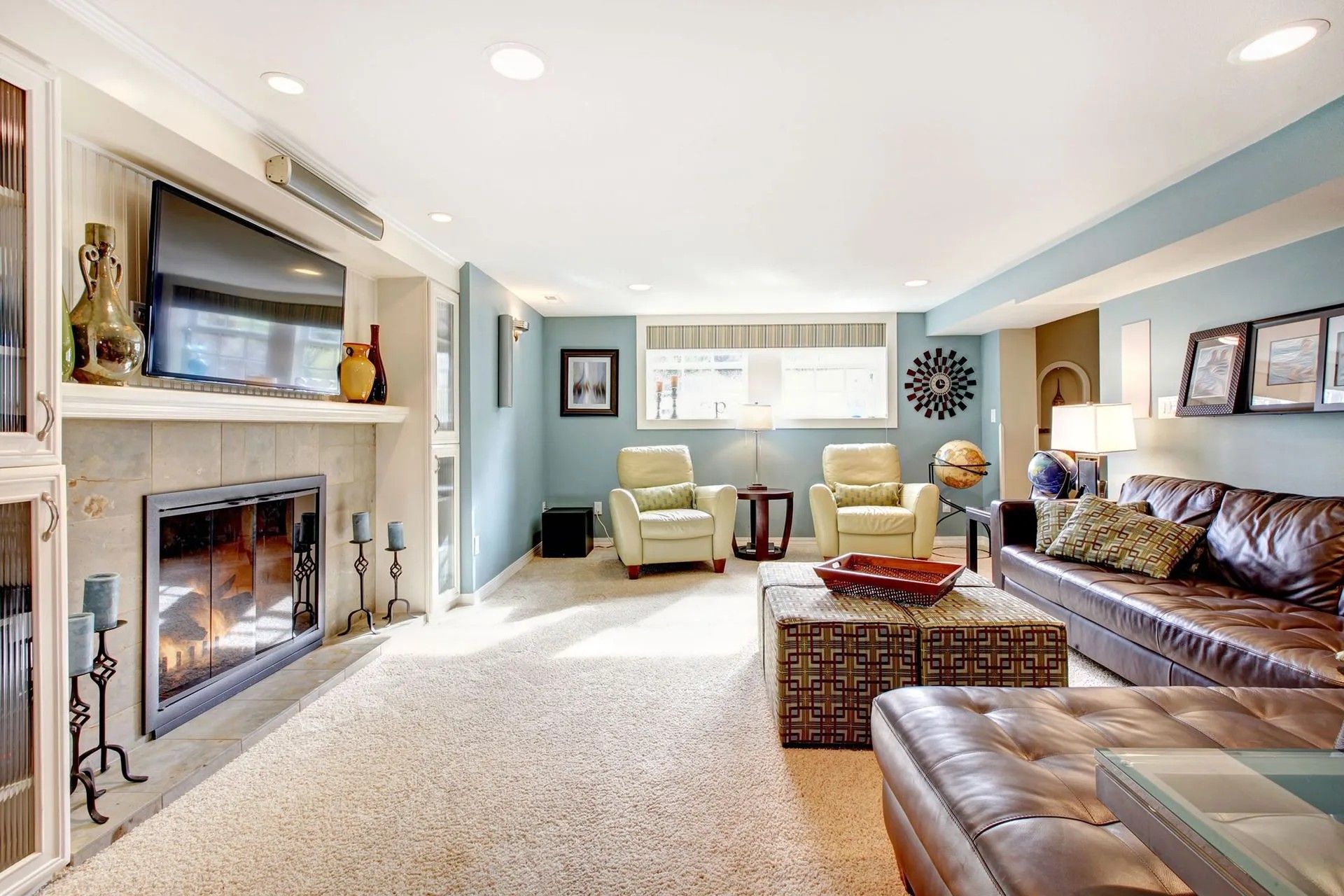 A cozy, light blue-walled living room with a fireplace, leather sofa, armchairs, and a large, textured rug.