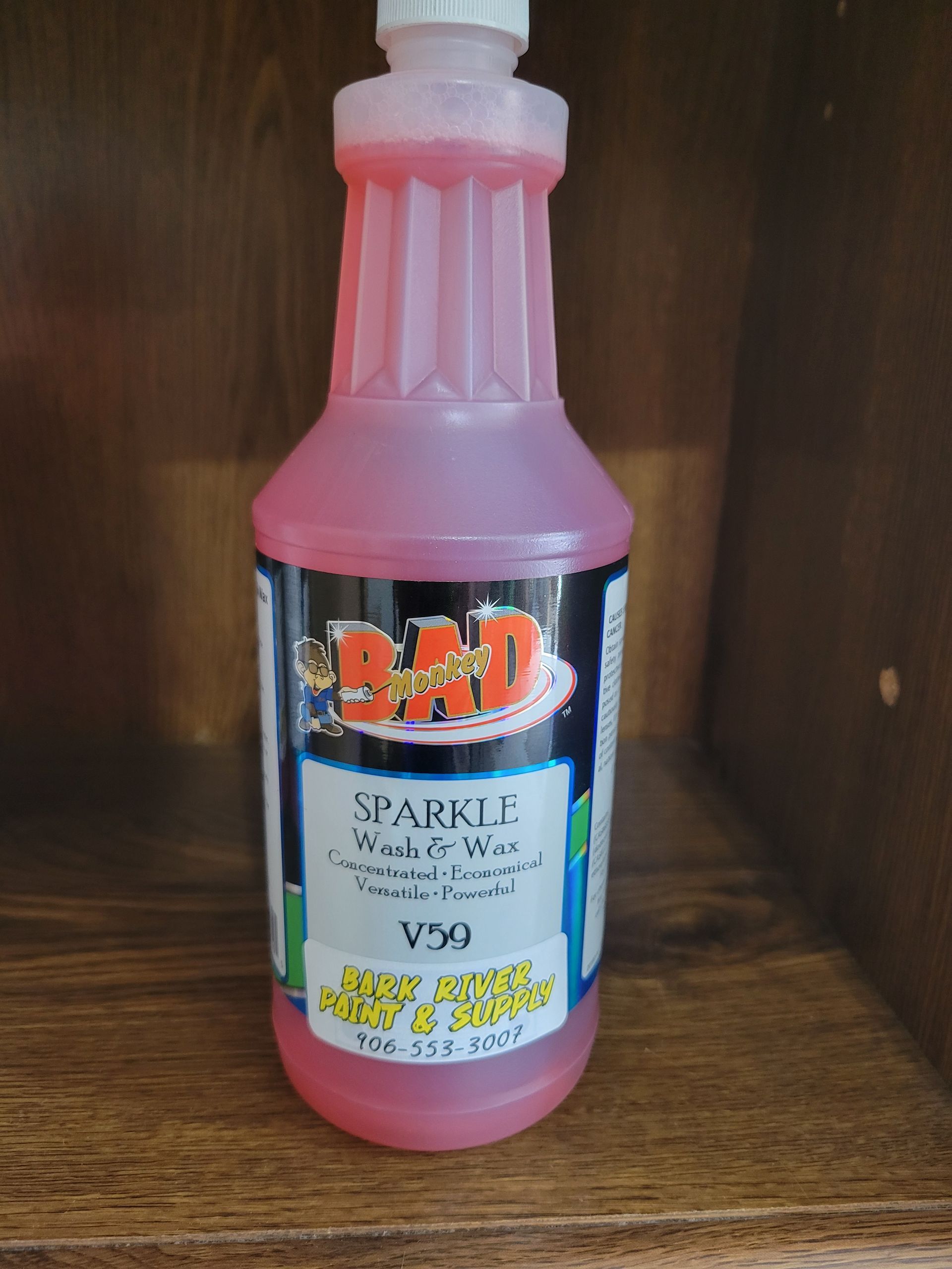 Pink bottle of syrup or sauce with a white cap on a wooden shelf