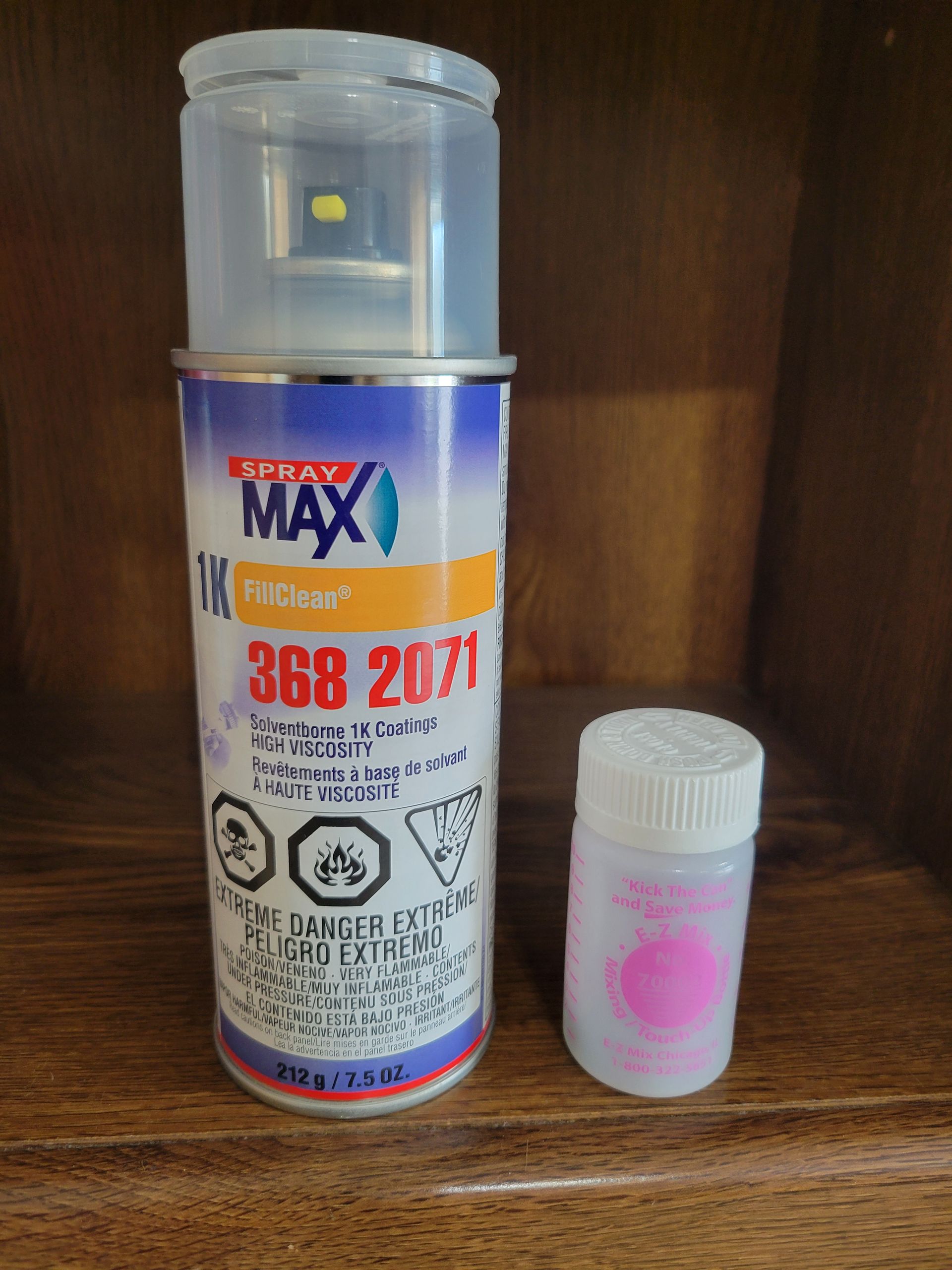 A blue-and-orange spray can beside a small pink pill bottle on a wooden shelf.
