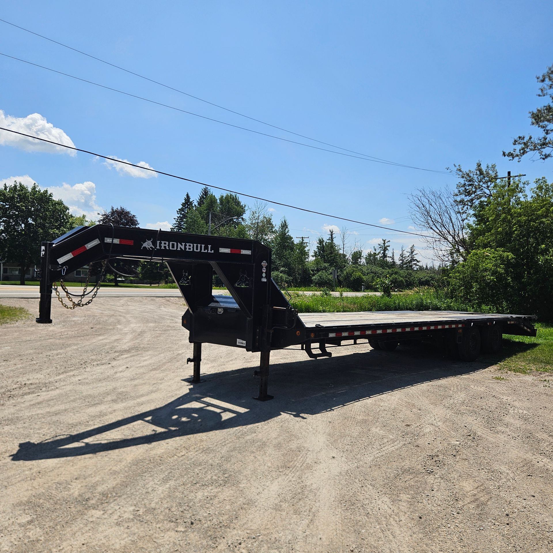 Black flatbed trailer parked on a gravel lot under a clear blue sky
