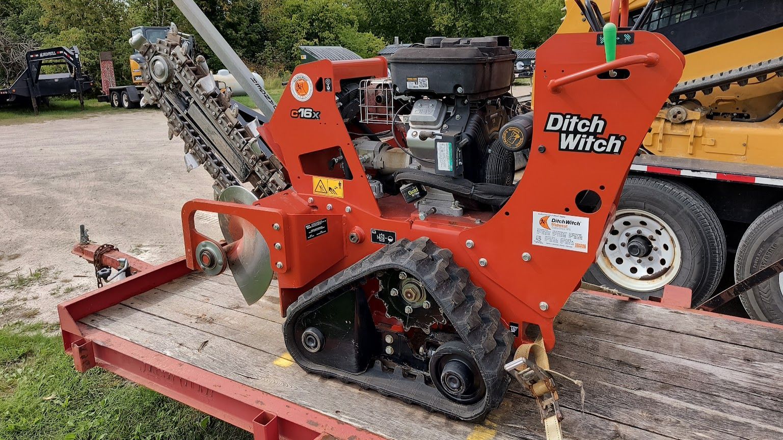 Orange Ditch Witch trencher on a flatbed trailer, with digging chain visible outdoors