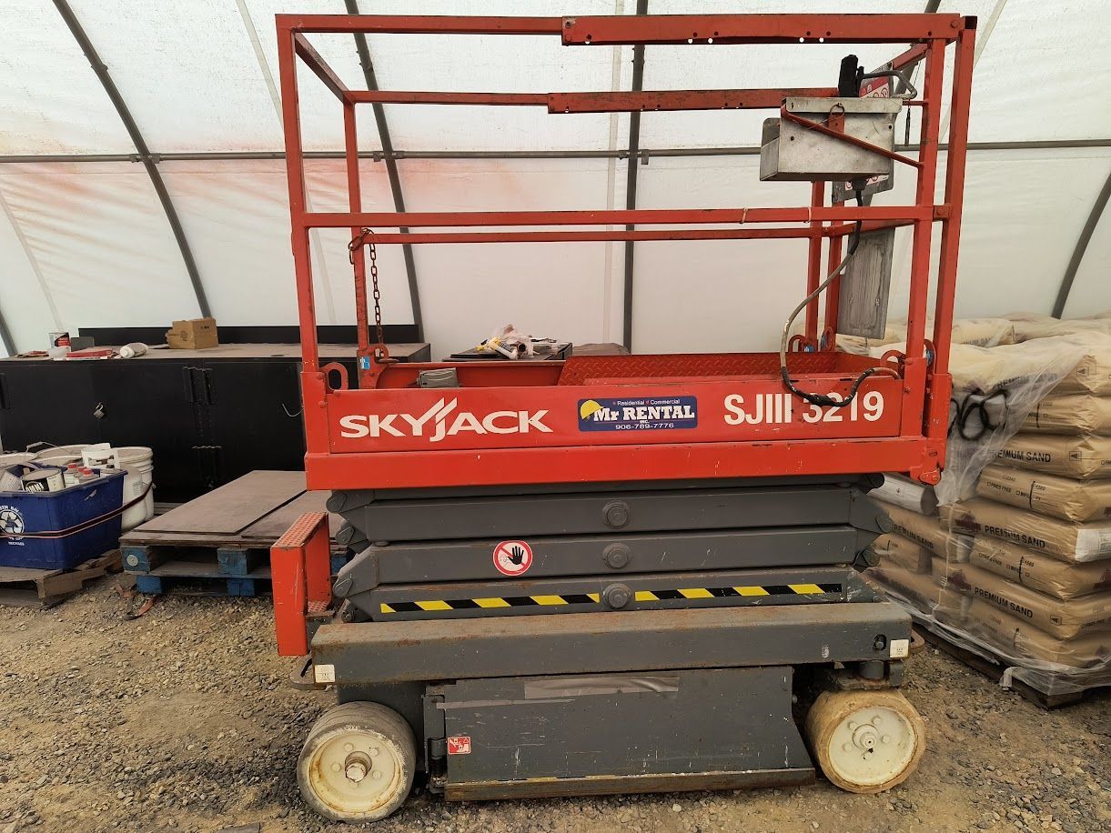 Red Skyjack scissor lift parked indoors on a warehouse floor