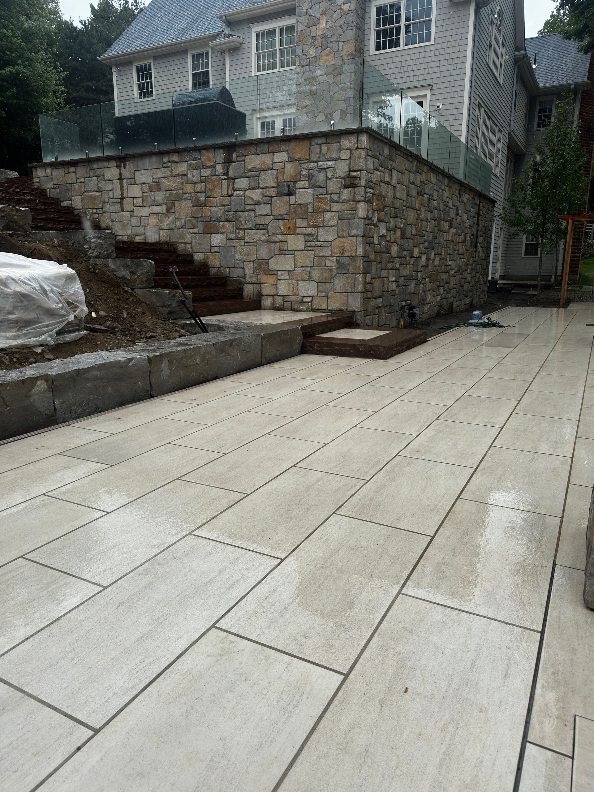 Stone-paved driveway beside a retaining wall and stone house, with a large white bag on the left.