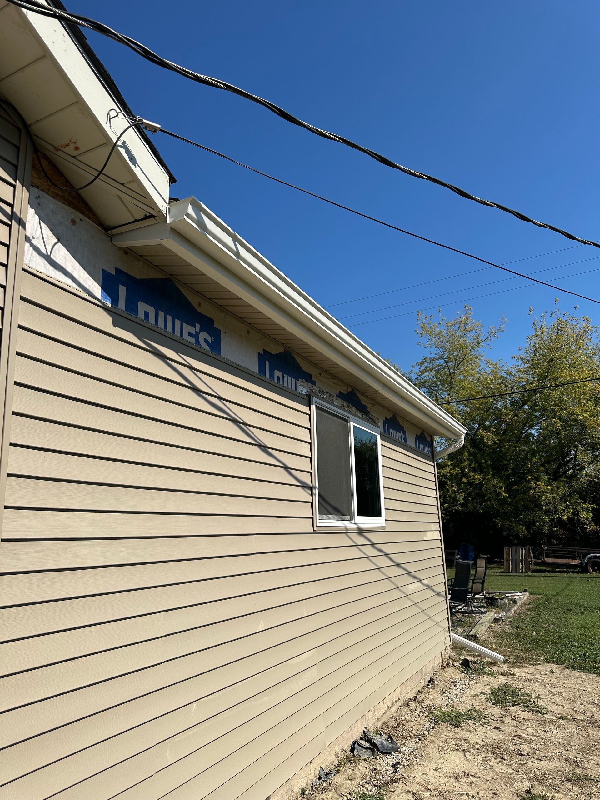 Side view of a house with tan siding and a new white window. Blue sky overhead.
