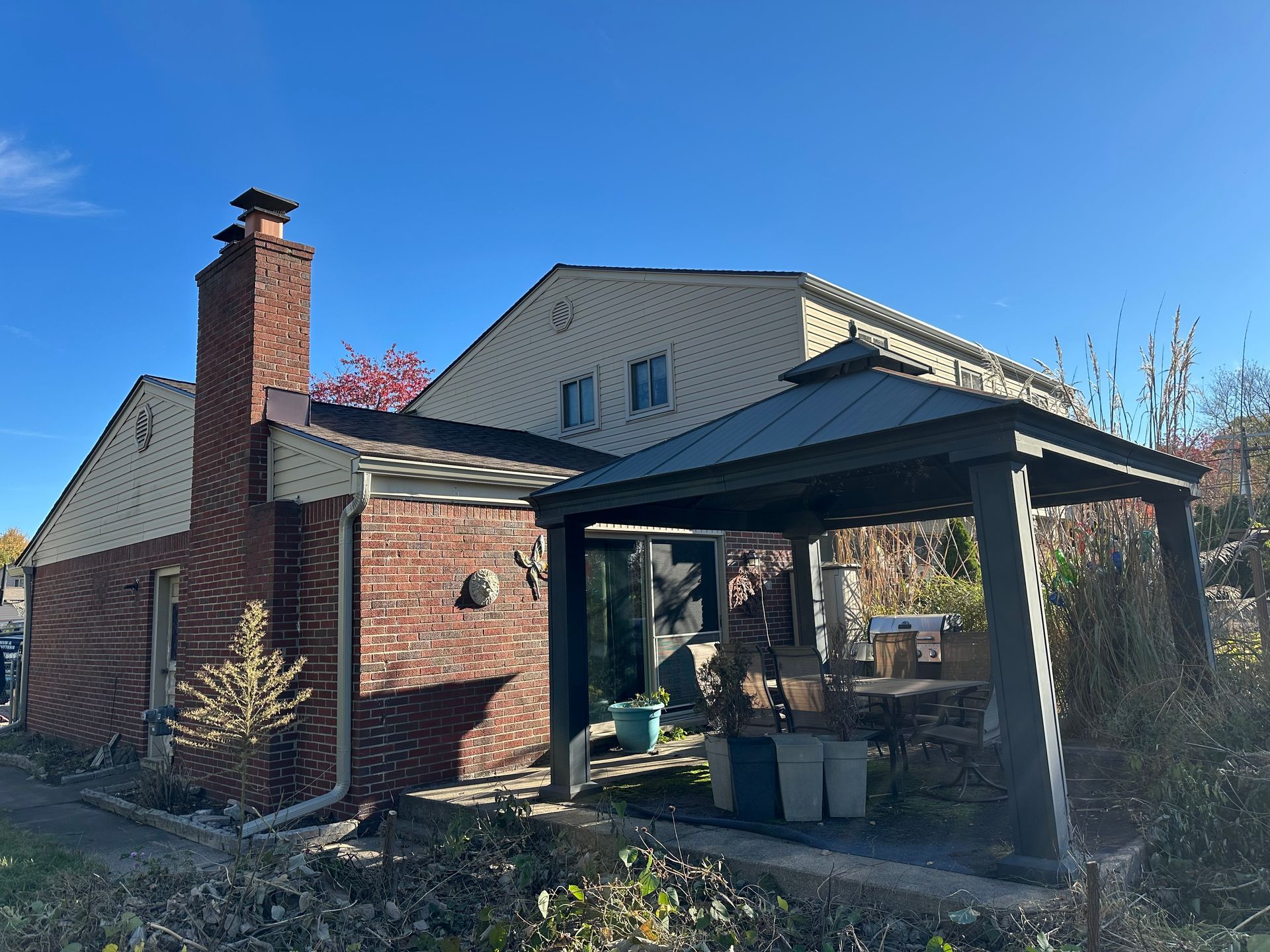 Brick house with chimney, a gazebo, and blue sky.