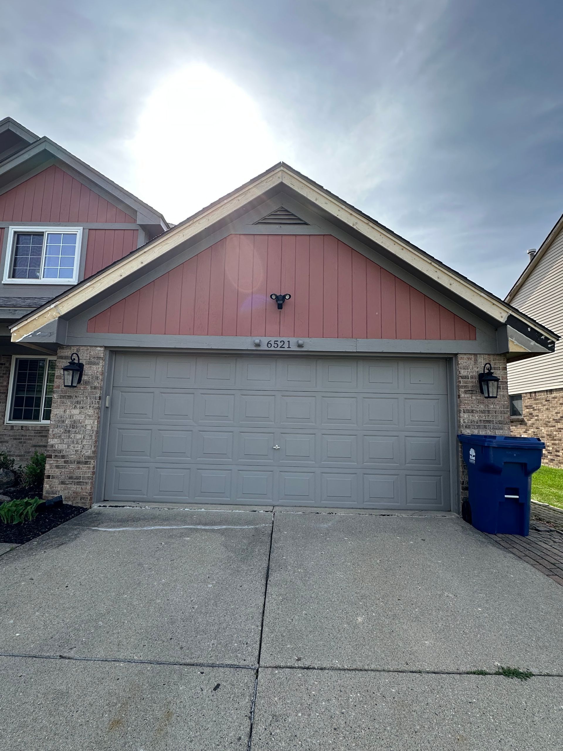 Garage with gray door, red siding above, and driveway.