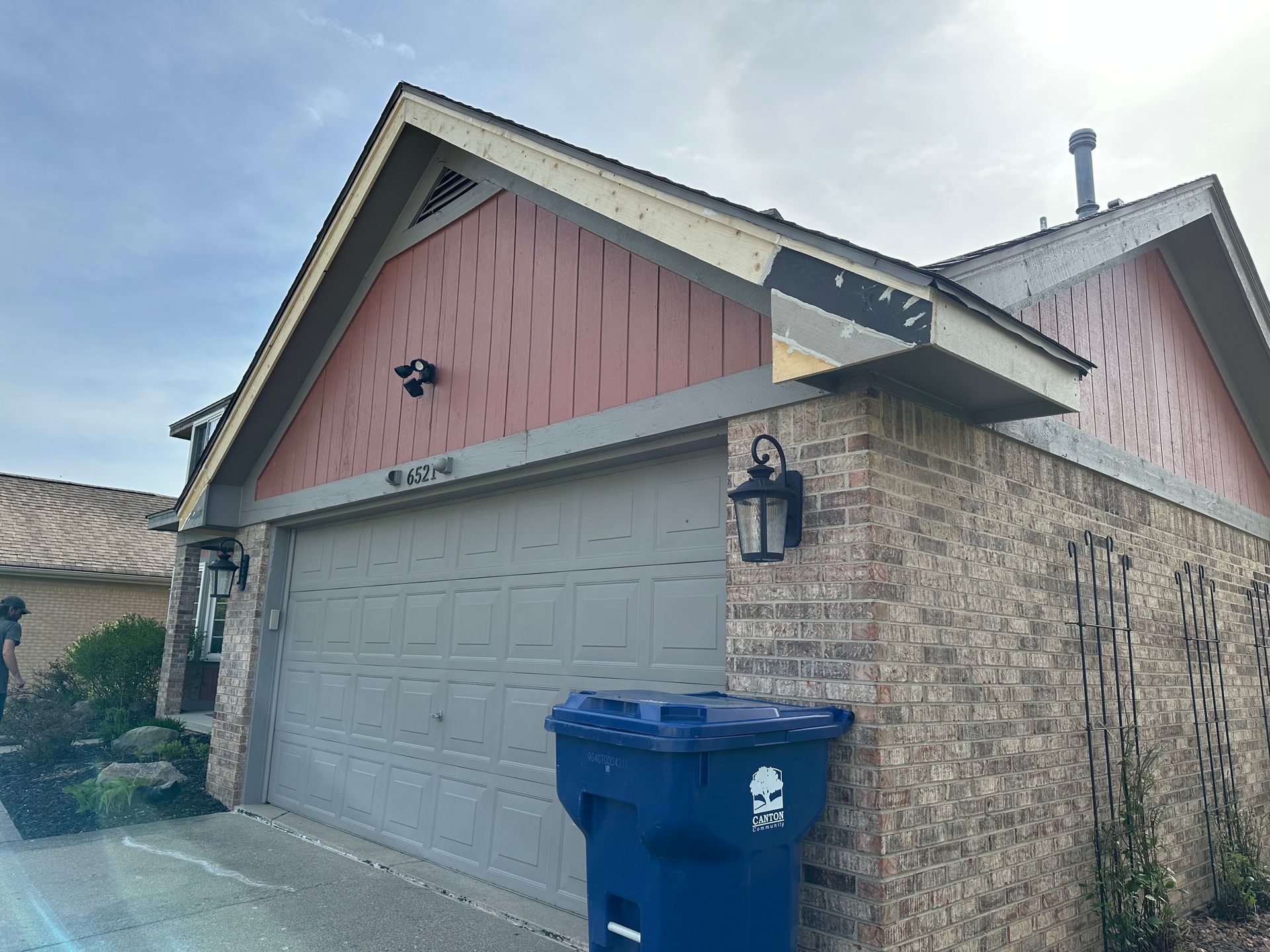 House with brick exterior, gray garage door, red siding, and blue trash can.